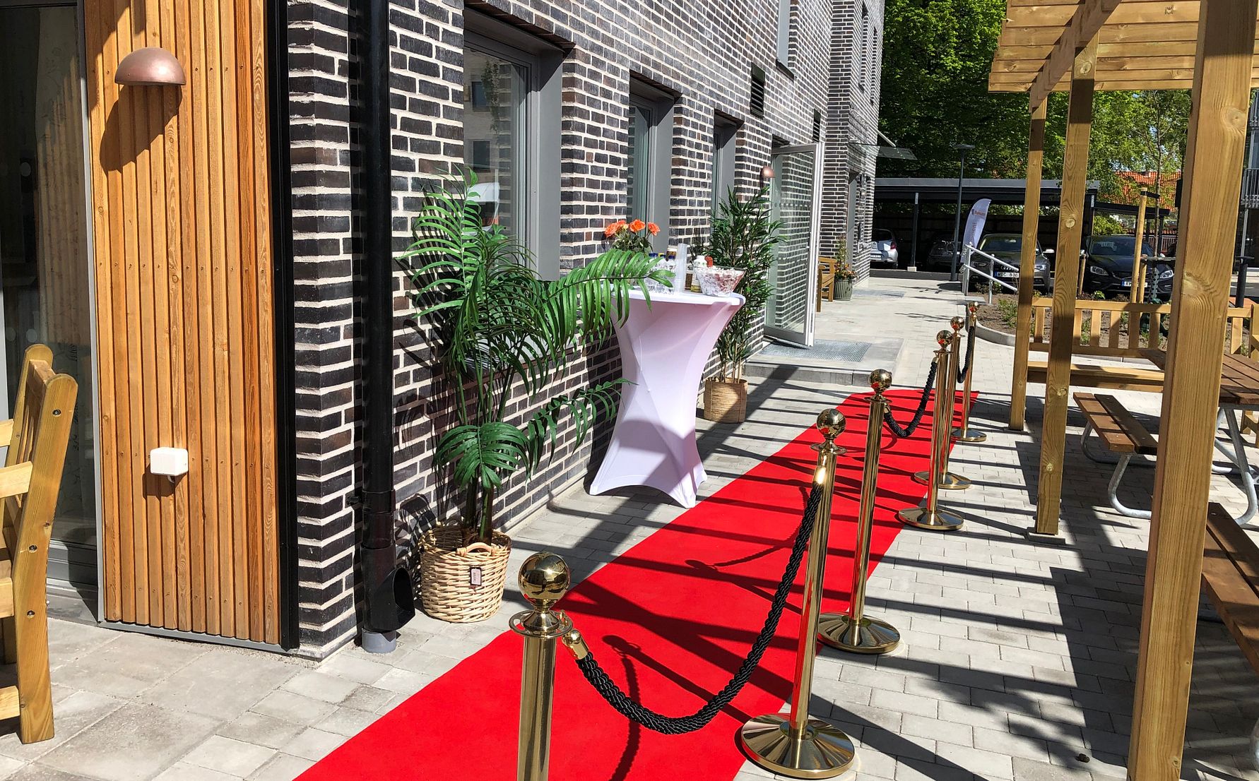 Röd matta med avspärrningar som leder till ett bord med dekorationer, vid en modern byggnad av tegel