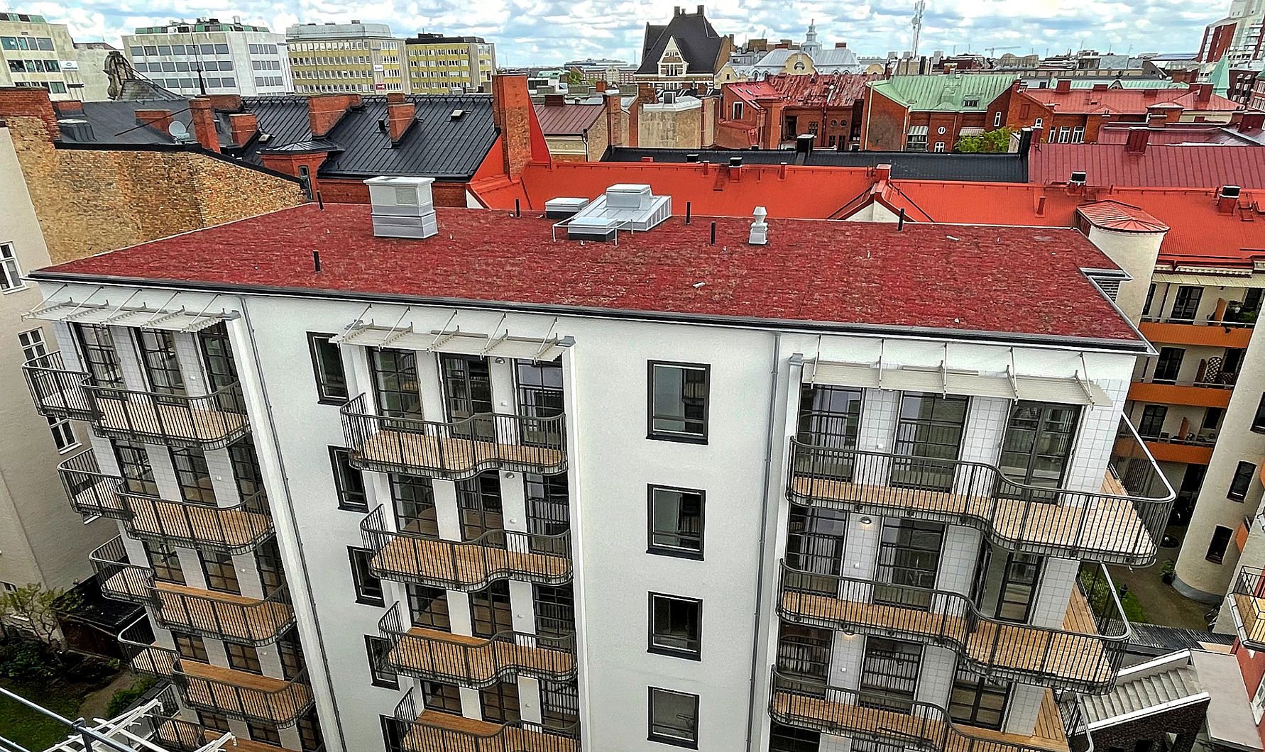 Flerbostadshus med vit fasad och röda tak, omgiven av andra byggnader i stadsmiljö