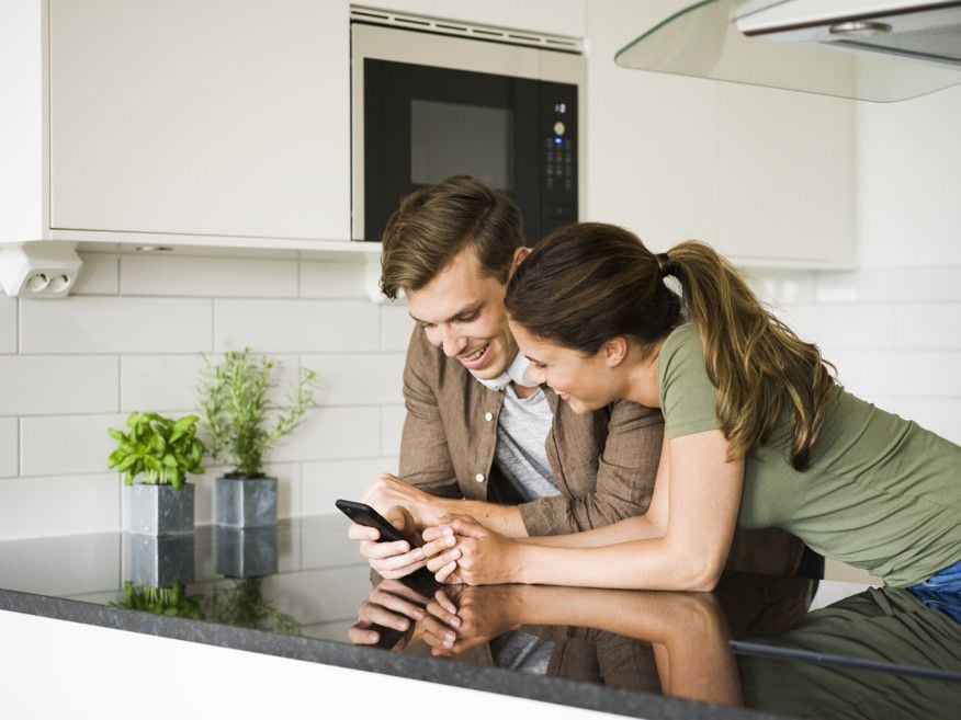 Två personer står vid en köksbänk i ett modernt kök och tittar på en smartphone