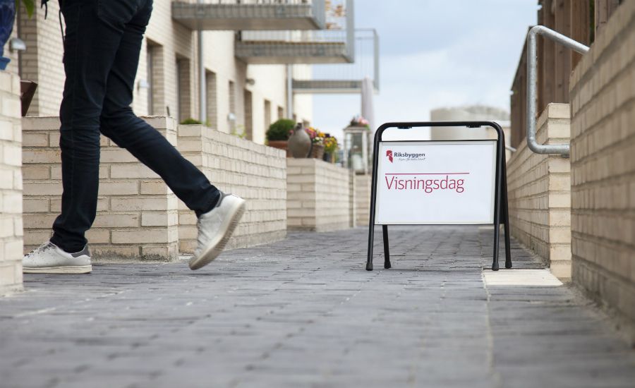Person som går på en stenlagd gång bredvid byggnader, med en skylt som visar "Visningsdag" placerad vid sidan av gången
