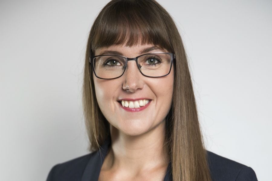 En person med långt brunt hår iklädd en mörk blazer, fotograferad mot en ljus bakgrund