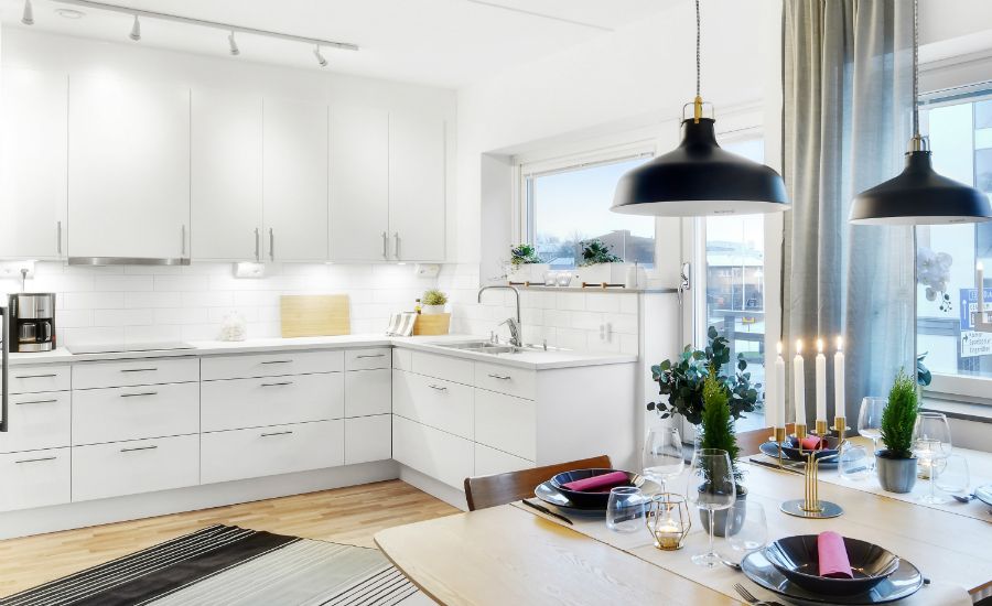 Ljust kök med vita skåp, trägolv och en matplats med dukat bord, levande ljus och gröna växter