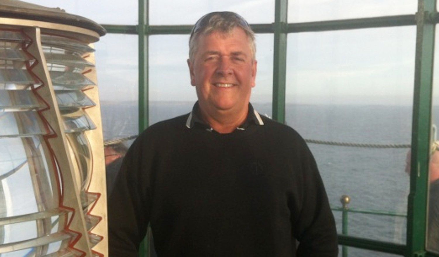 Man i svart tröja står framför ett fönster i en fyr med utsikt över havet