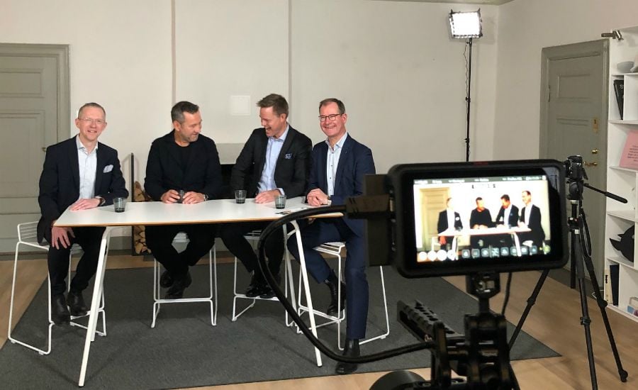 Fyra personer sitter vid ett bord i ett ljust rum, framför en kamera på ett stativ