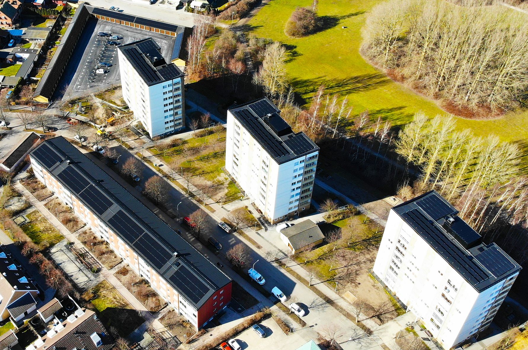 Flerbostadshus med solpaneler på taken, omgivna av grönområden och träd i ett bostadsområde