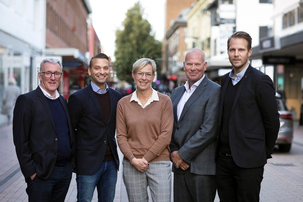 En grupp personer står på en gågata med butiker och byggnader i bakgrunden