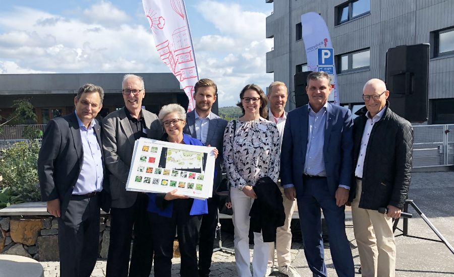 En grupp människor poserar utomhus framför en byggnad med flaggor och en bildhållare med tryckt material