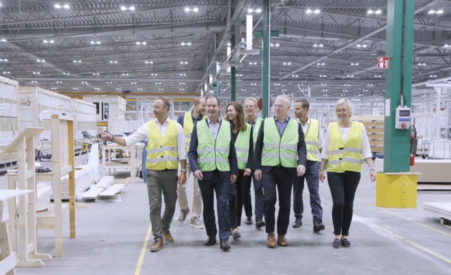 Personer i reflexvästar som går genom en fabrikshall med maskiner och material runtomkring