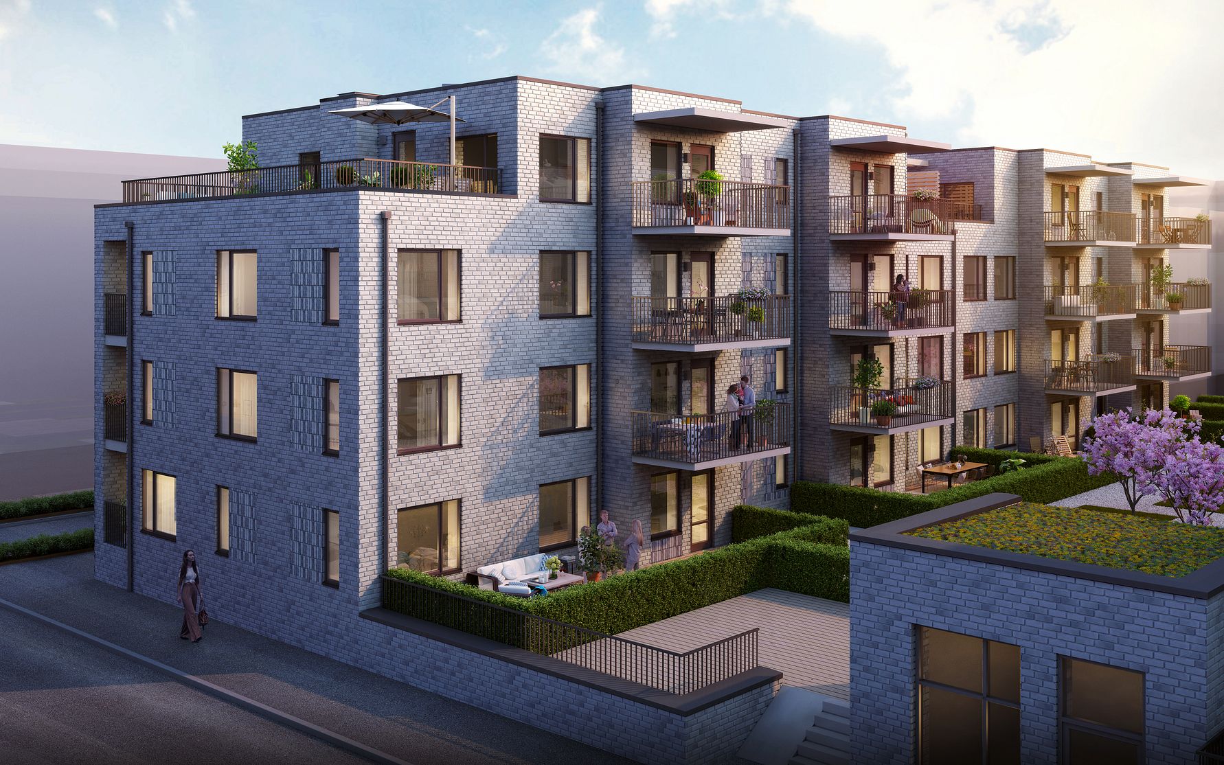 Modernt flerfamiljshus i grå tegel med balkonger, grönområden och utemöbler, beläget intill en gata under en klar himmel