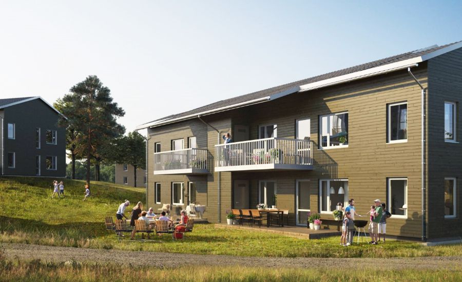 Modern bostadsbyggnader med träfasad, människor som umgås utomhus vid bord och en grön gräsmatta under en klar himmel