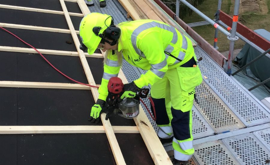 Byggarbetare i neonfärgade arbetskläder som sågar trä med en elektrisk såg på en byggarbetsplats