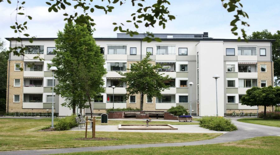 Flerbostadshus med flera våningar, omgiven av grönområden, träd och gångstigar
