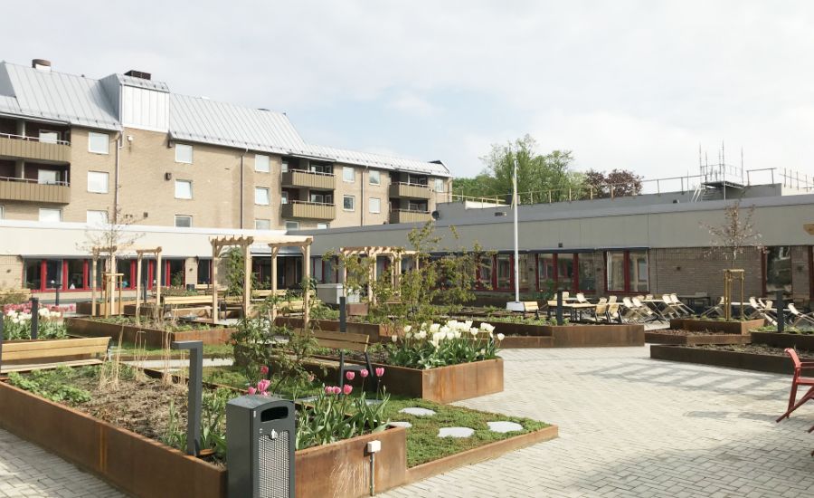 Innergård med planteringslådor, blommor, träd och sittplatser omgiven av flerbostadshus