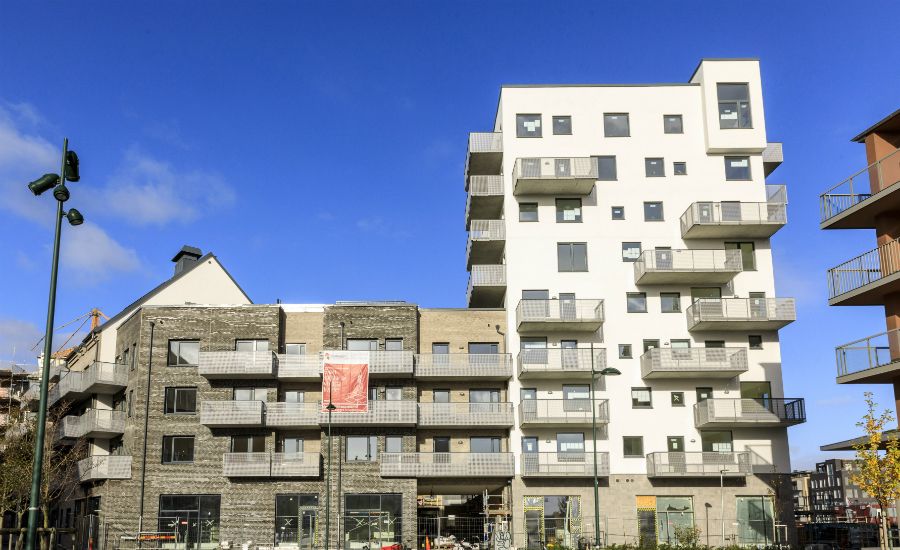 Modern flerfamiljshus med fasader av tegel och ljus puts, omgivet av byggnadsställningar och en klar blå himmel