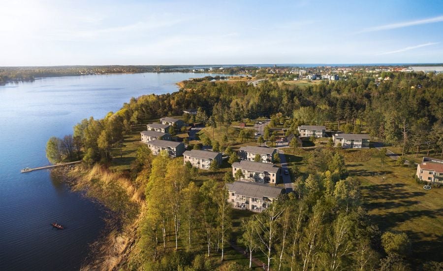 Flygvy över en naturskön bostadsområde vid en sjö med omgivande skog och klarblå himmel