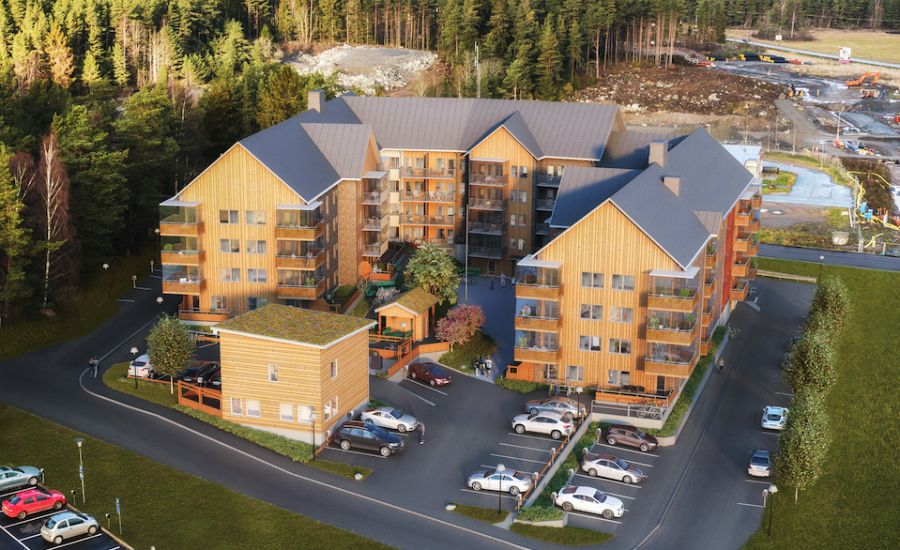 Luftvy av ett bostadsområde med flerfamiljshus i trä, omgärdat av parkeringsplatser och skog