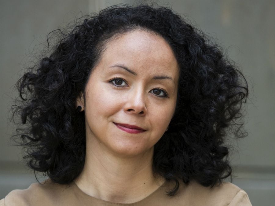 Person med lockigt mörkt hår som bär en beige topp, fotograferad framför en neutral bakgrund