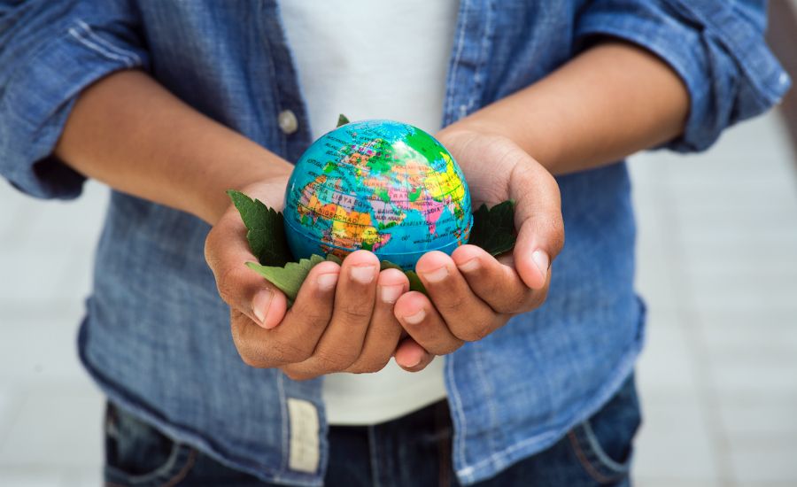 Händer som håller en liten jordglob med gröna blad, personen bär en blå jeansskjorta