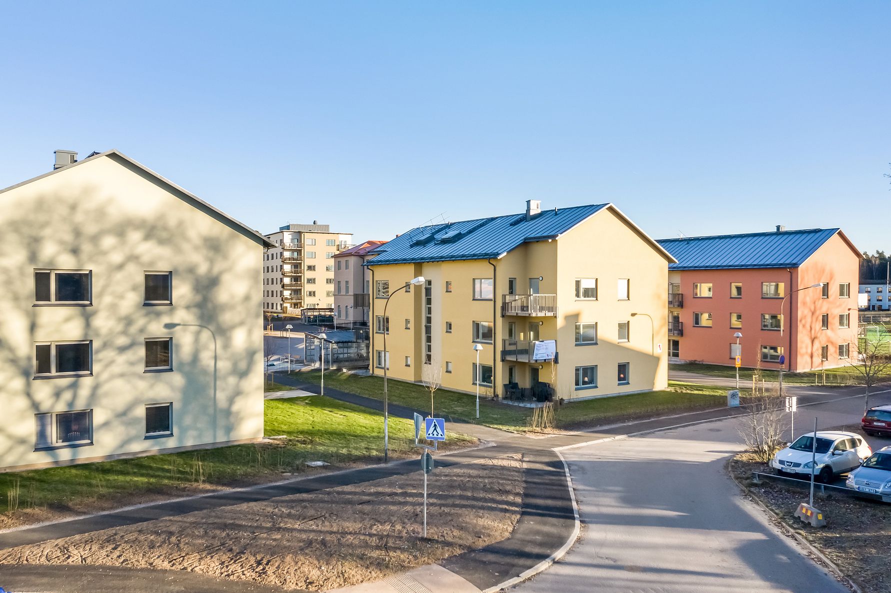 Bostadshus i ett kvarter med moderna flerfamiljsbyggnader, grönområden och asfalterade vägar under en klarblå himmel