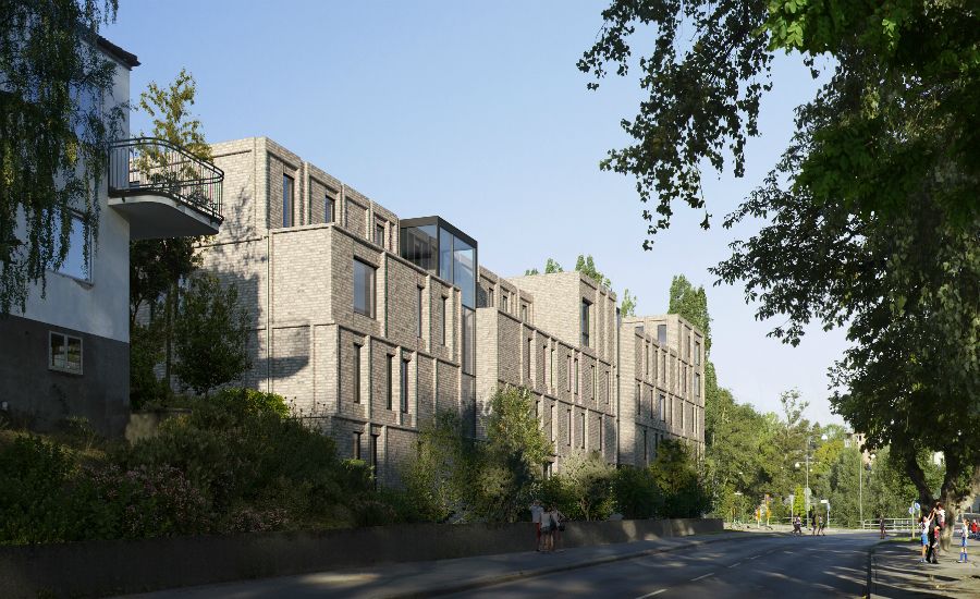 Modernt flerfamiljshus i tegel med grönska och träd längs en lugn gata