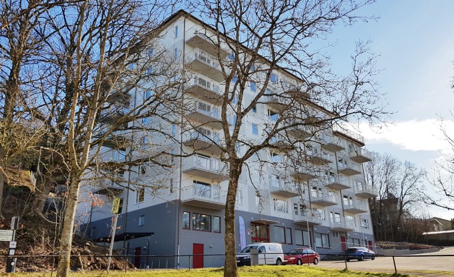 Flerbostadshus i modern stil med vita fasader och balkonger, omgiven av träd och bilar parkerade framför byggnaden
