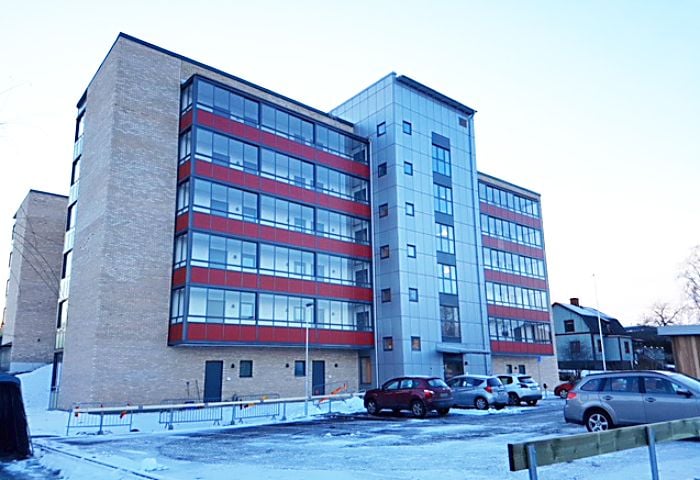 Kontorsbyggnad med glasfasad och röda detaljer, omgiven av parkerade bilar och ett snötäckt område