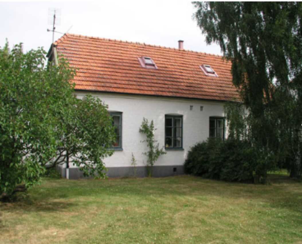 En vitputsad villa med brunt tegeltak och grönskande trädgård, omgiven av träd och gräsmatta