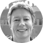 Porträtt av en leende kvinna med kort hår framför en byggnad, i svartvitt