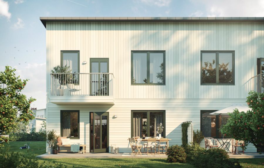 Modernt tvåvåningshus med vit fasad, balkong och stora fönster, omgiven av en trädgård med grönska och utemöbler