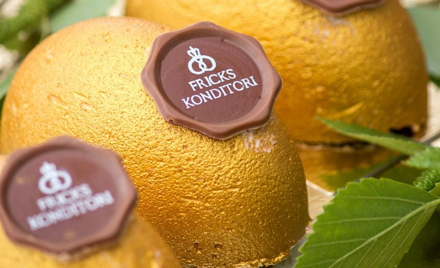 Gyldene dessertkupoler med chokladstämpel från Fricks Konditori, omgivna av gröna löv
