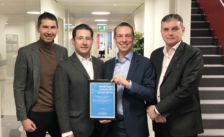 Fyra personer står i en kontorsmiljö, en av dem håller i ett diplom med blå text