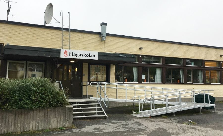 En byggnad med en gul fasad, skylt med texten "Hagaskolan", ramper och entrédörrar