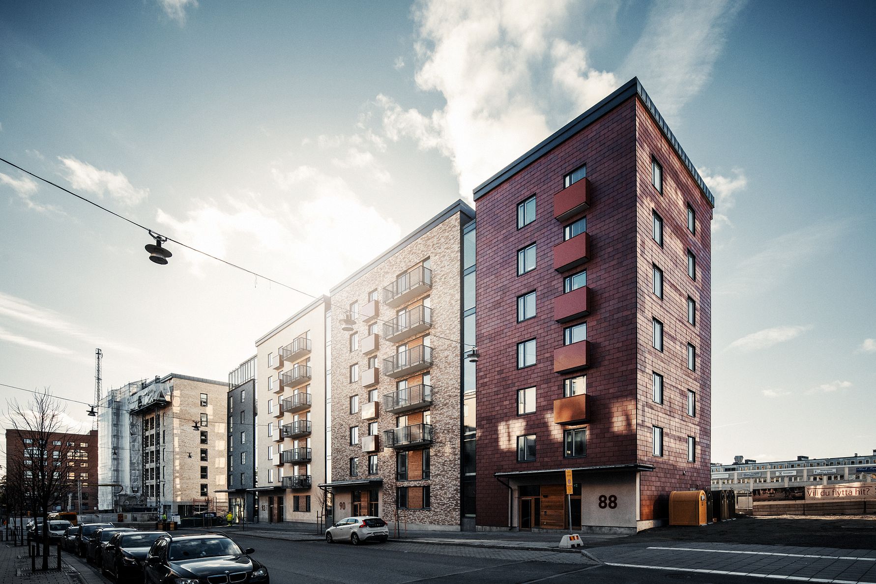 Flerbostadshus längs en gata, med moderna fasader och parkerade bilar på sidan