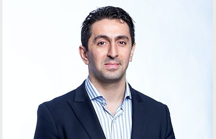 En person i en mörkblå kostym och randig skjorta mot en ljus bakgrund