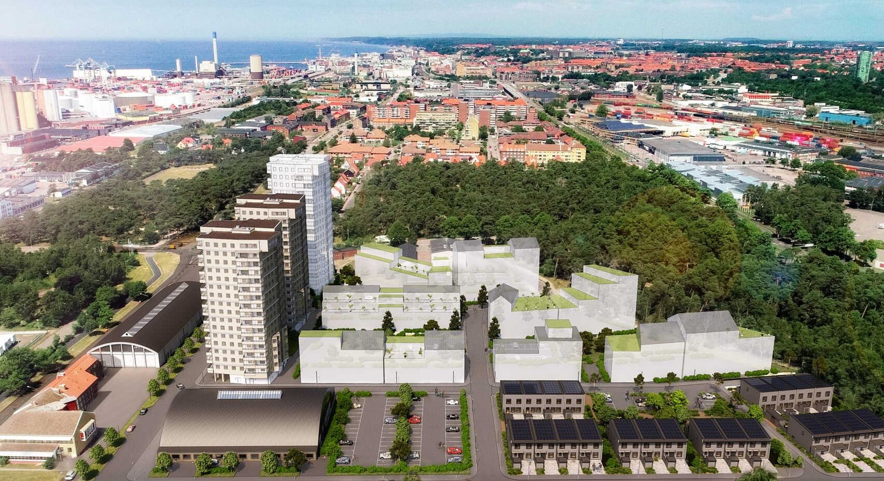 Flygbild över en stadsdel med höghus, mindre byggnader, grönområden och en hamn i bakgrunden