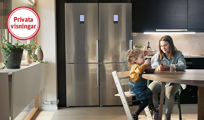 Kök med modern inredning, ett stort kylskåp i rostfritt stål, och ett runt bord där två personer sitter