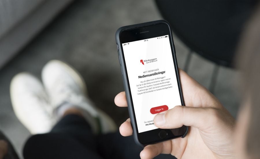 En person håller en smartphone som visar en skärm med text och en röd knapp för inloggning