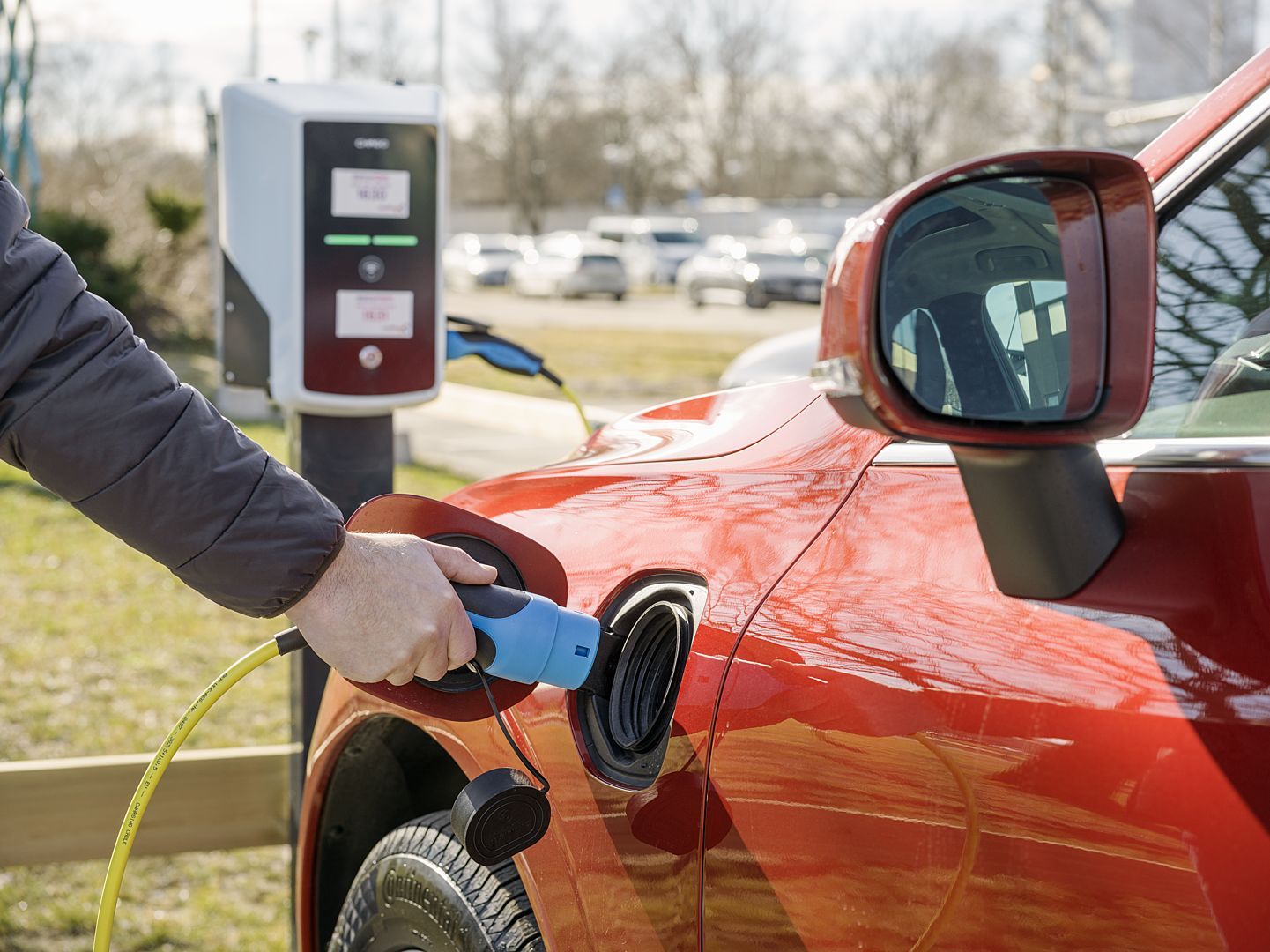Person laddar en röd elbil vid en offentlig laddstation utomhus