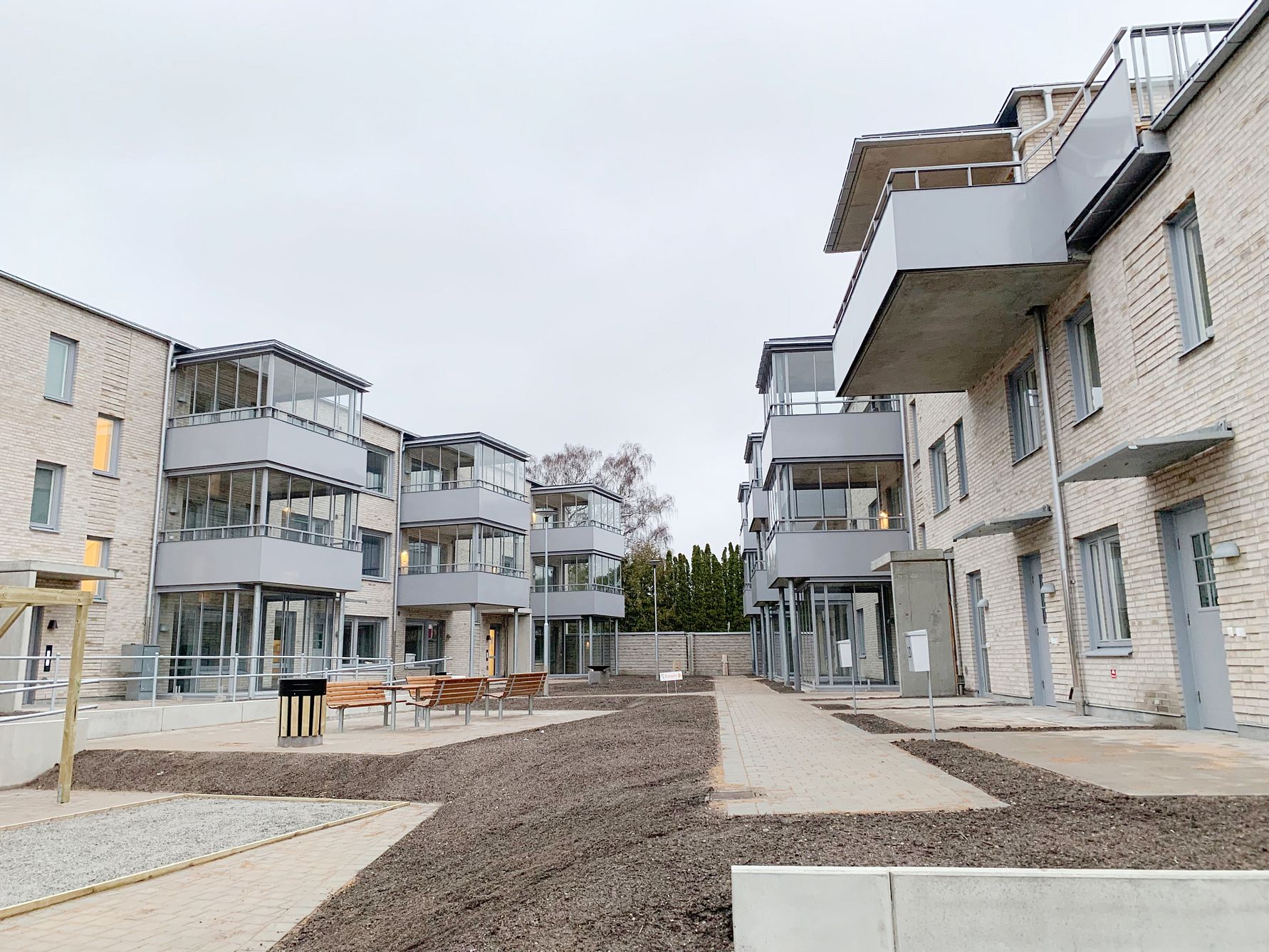 Flera moderna lägenhetsbyggnader med balkonger, grå fasader och en innergård med bänkar och gångvägar