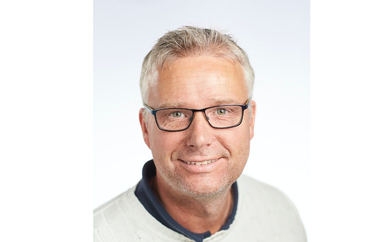 Man i vit tröja med mörkblå krage mot en vit bakgrund