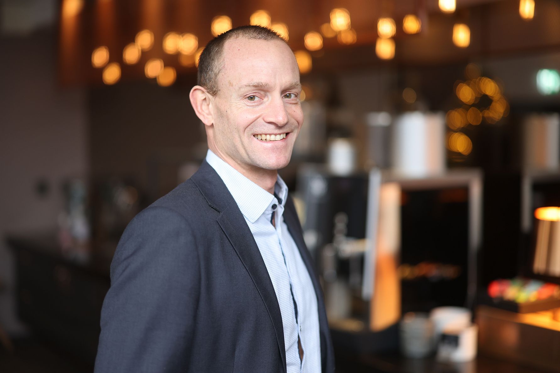 En man i kostym står i en modern miljö med suddig bakgrund och varm belysning