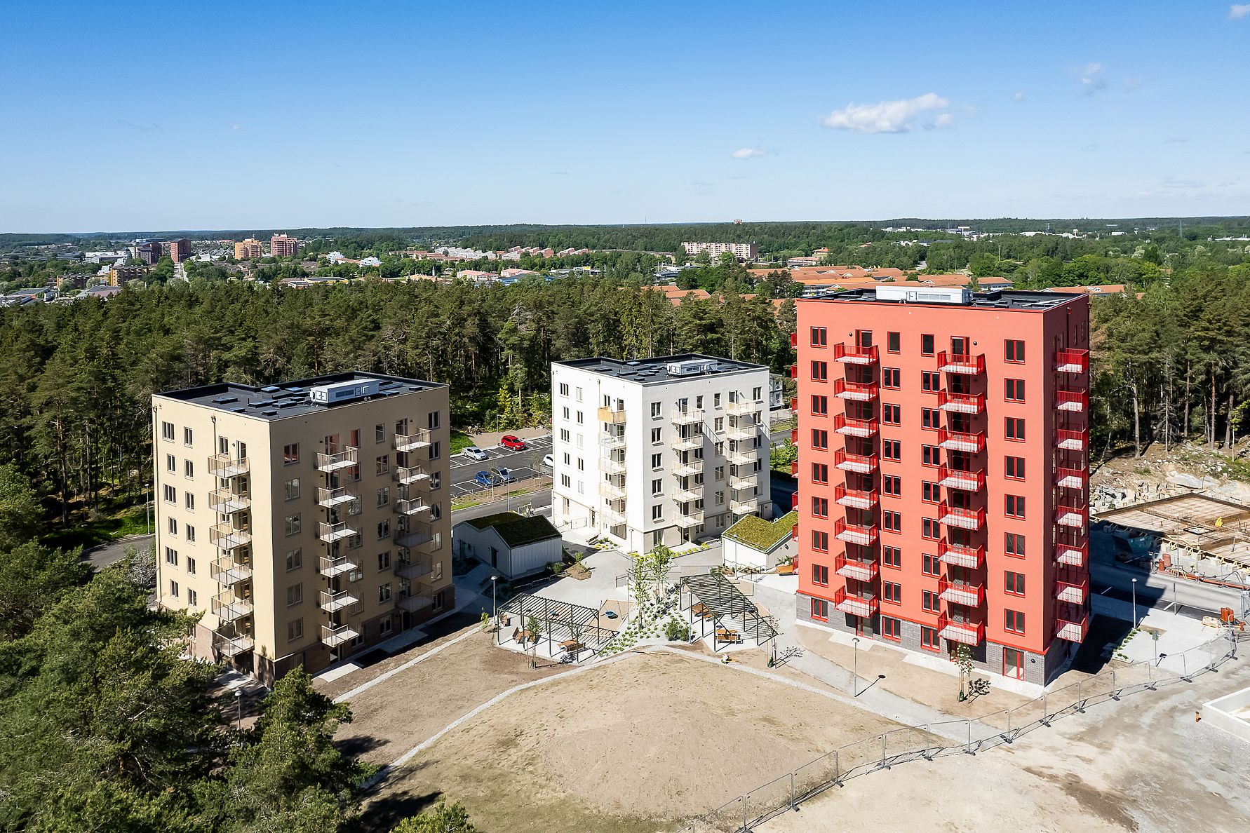 Flerbostadshus i modern stil, omgivna av grönska och öppna ytor under en klar blå himmel