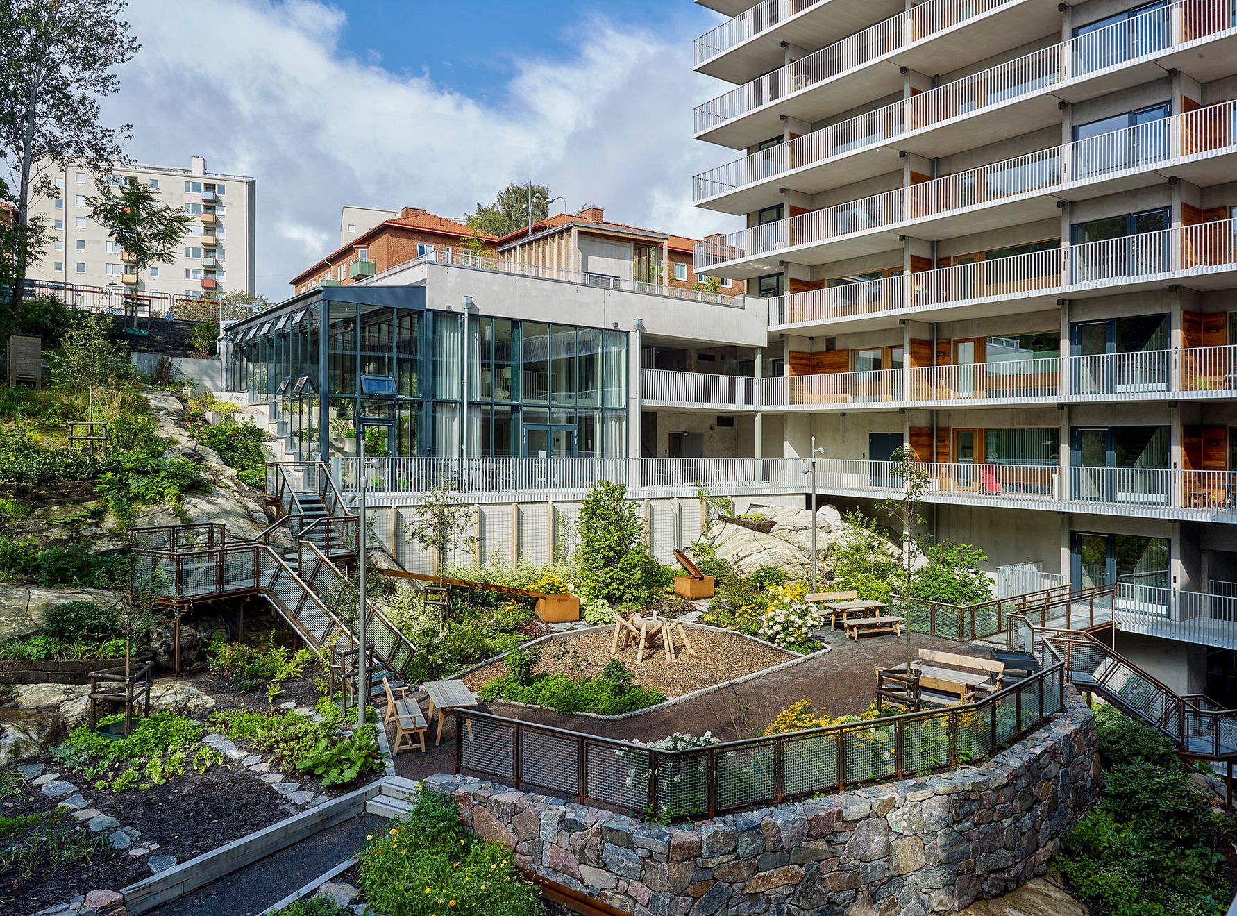 Flerbostadshus med moderna balkonger, grönskande trädgård och utsikt över parkområde under en klar himmel