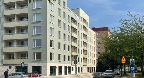 Modern flerfamiljshus med ljusa fasader, balkonger och parkeringsplatser i förgrunden. Träd och en blå himmel i bakgrunden