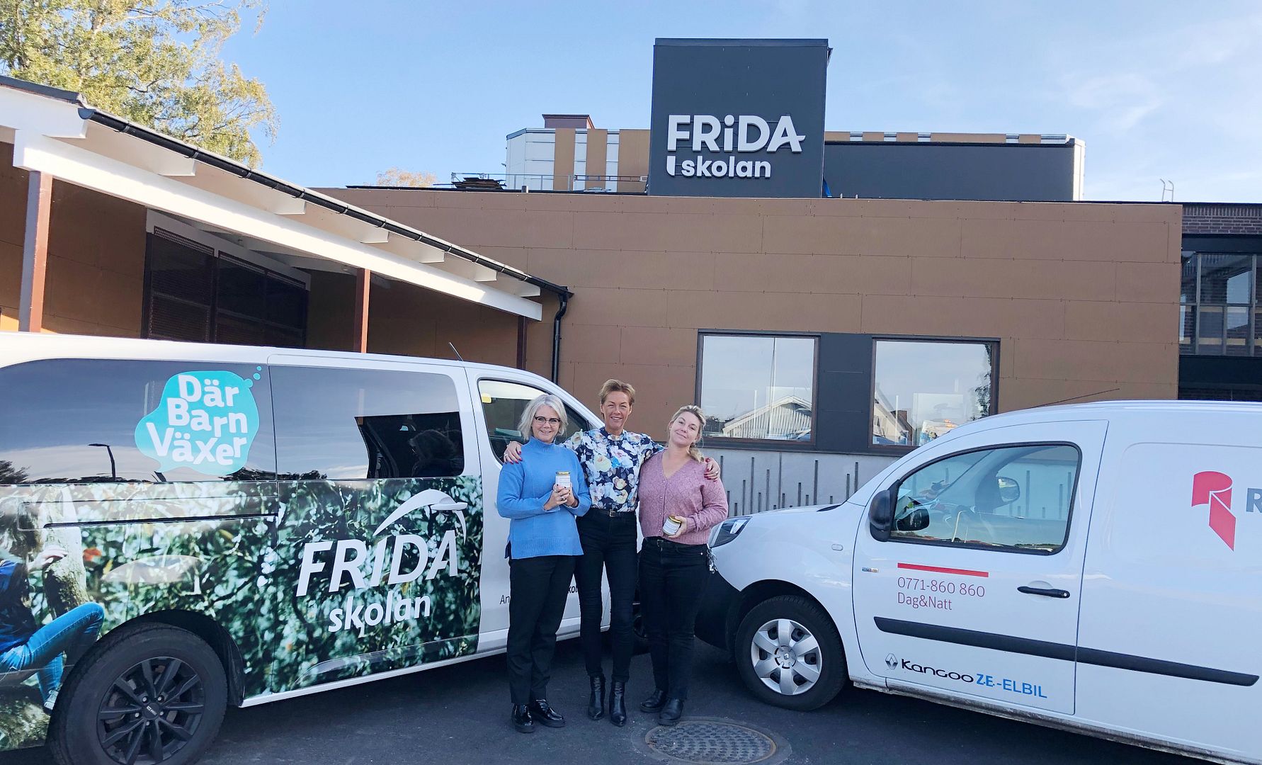 Tre personer står framför två vita skåpbilar och en byggnad med texten "Fridaskolan" på fasaden