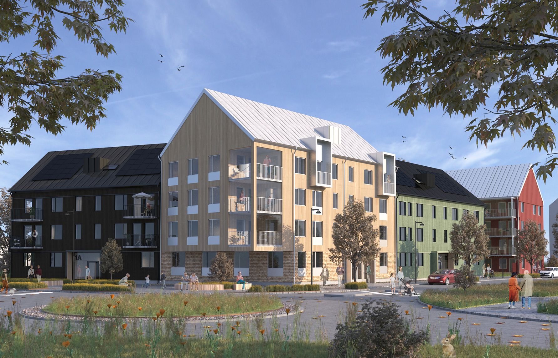 Nybyggda flerfamiljshus med olika fasadfärger vid en grönskande rundel under en klar blå himmel