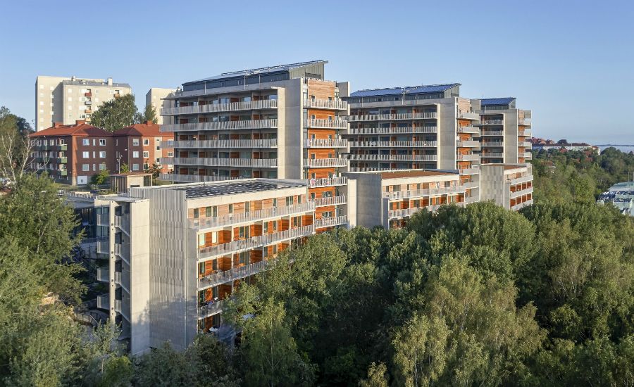 Flerbostadshus omgivna av grönska med utsikt över angränsande byggnader under en klar blå himmel