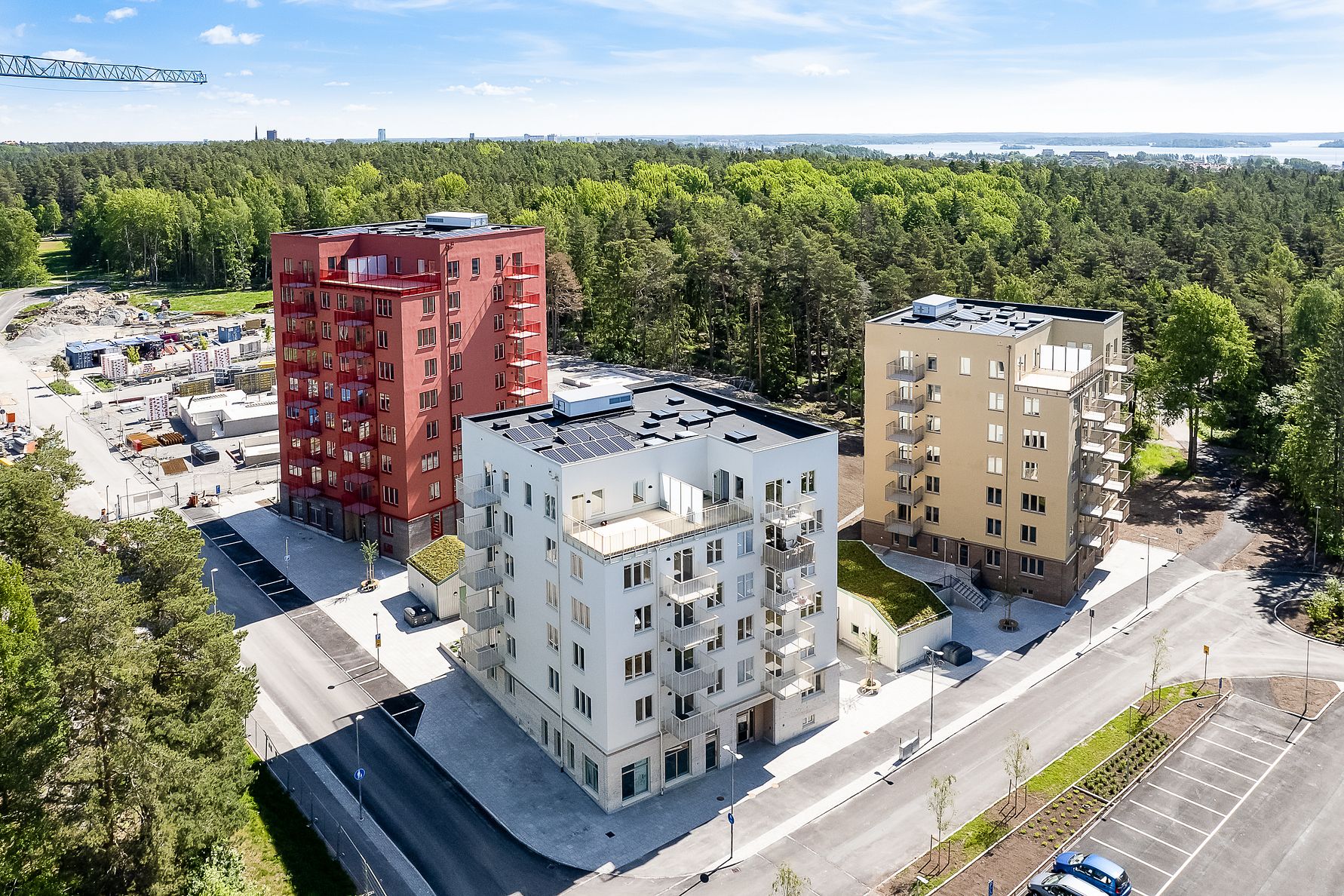 Flerbostadshus i varierande färger, omgivna av skog och grönska med parkeringsplatser i förgrunden