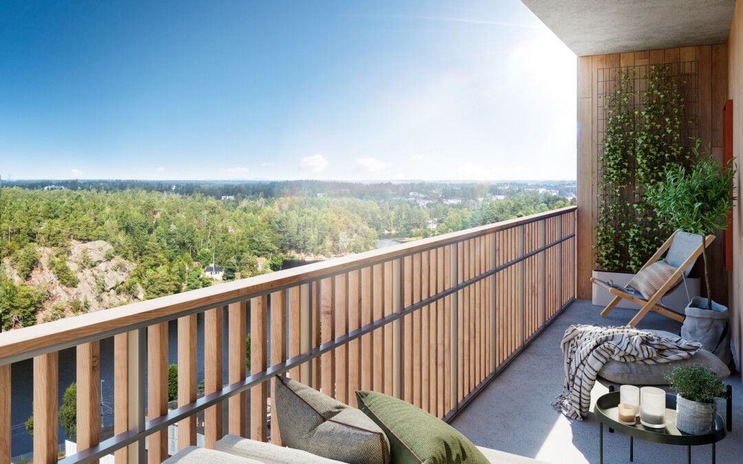 Balkong med trästaket, utsikt över skogsklädda omgivningar och klarblå himmel. Möbler inkluderar stolar, bord och gröna växter