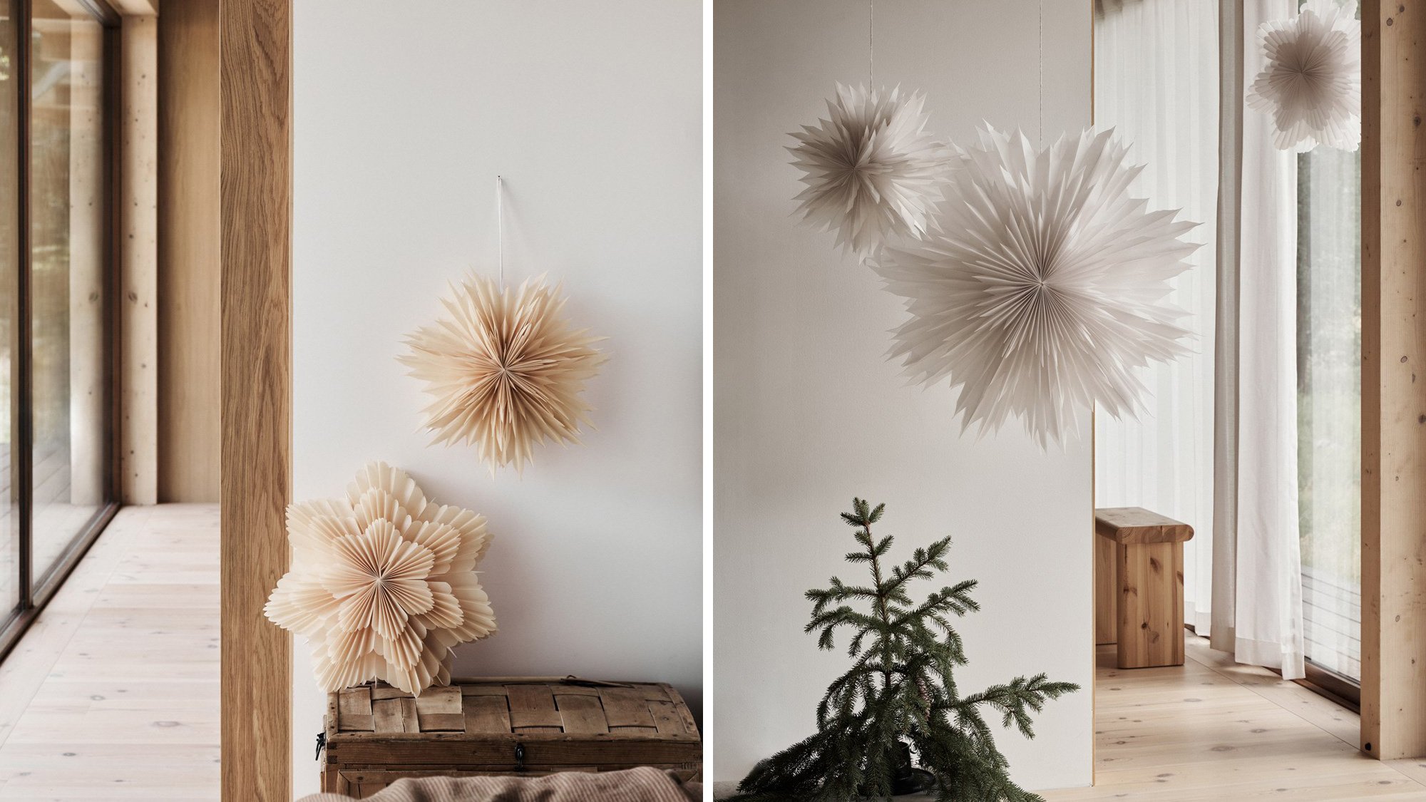 Dekorativa pappersstjärnor i beige och vit hänger i ett modernt trähus, med ett litet barrträd i förgrunden och ljusinsläpp från stora fönster